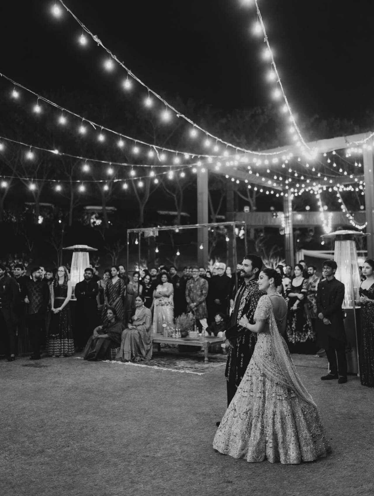 Several monochrome shots show the couple laughing, dancing and soaking in love, while vibrant stage pictures feature high-energy dance performances. A family portrait from the beautifully lit outdoor location captures the couple standing amid their loved ones